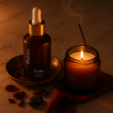 Bottle labeled 'Phenxx Evoke Alcheme oil' next to a lit candle on a warm-toned background